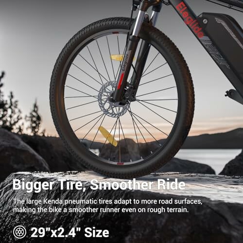 Mountain bike with large Kenda tire on rocky terrain.